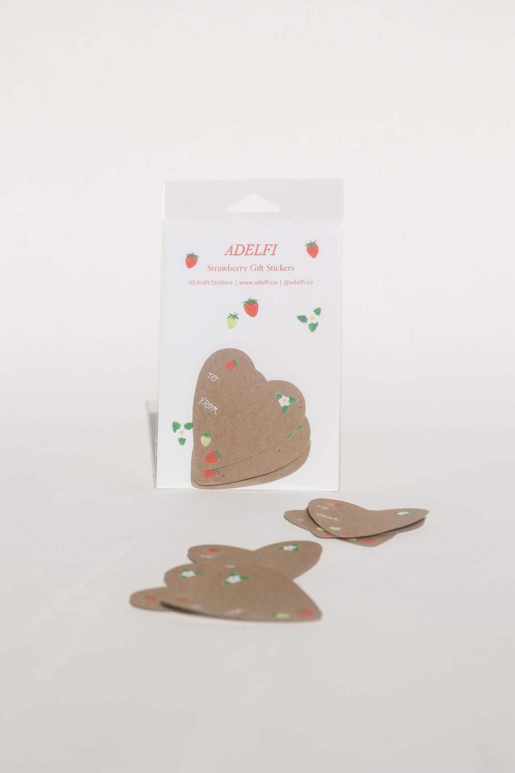 This Gift Sticker is heart-shaped with a red strawberry in the upper left hand corner, a green and red strawberry at the bottom, and a white flower with three leaves in the upper right corner, with the words "To" and "From" written in cursive in the center left.