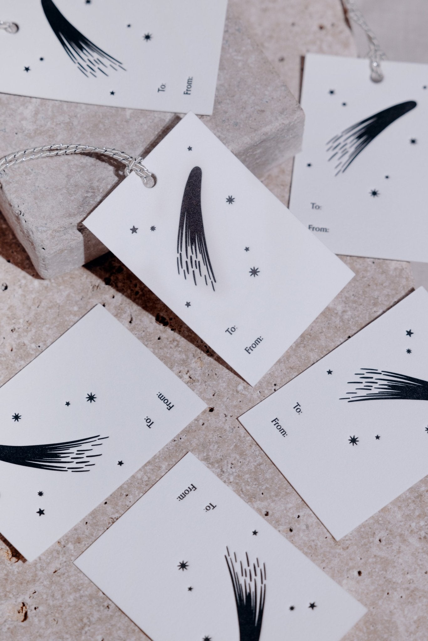 Adelfi letterpressed gift tags scattered across a gray stone background.