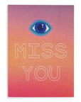 Greeting card with the symbol of an eye followed by the words "Miss You" in white hollow font on a gradient purple, orange and red cardstock. Shown against a white background.