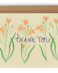 Four stems of orange forest flowers reaching upward cover the card nearly top to bottom horizontally, with the words "Thank You" going through the center of them in black ink. This design is printed on a cream colored background. Shown with Kraft envelope.