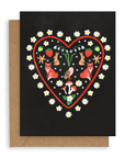 A red heart-shaped outline surrounded by white flowers with two foxes facing away from each other, two rabbits facing opposite above them, and an owl in the middle with forest flowers above, red mushrooms and white flowers below, and strawberries/flowers above. Printed on a black background. Shown with Kraft envelope.