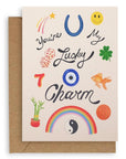 Cream colored card with various lucky items on the front: penny, goldfish, four leaf clover, dice, the number seven, bamboo plant, yin and yang, rainbow, horseshoe, shooting star, and smiley face with the words "You're My Lucky Charm" printed on cardstock. Shown with kraft envelope.