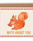 A large squirrel holding a heart positioned above the words "nuts about you" in orange font. Red hearts line each side of the card. Shown with kraft envelope.