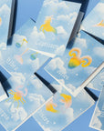 Adelfi Horoscope cards have a light blue background with white clouds and each of the twelve horoscope symbols painted in pastel rainbow colors.