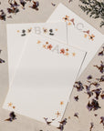 A, B, and C pressed flowers monogrammed notecards on cardstock against a raw canvas background with varying purple flowers.