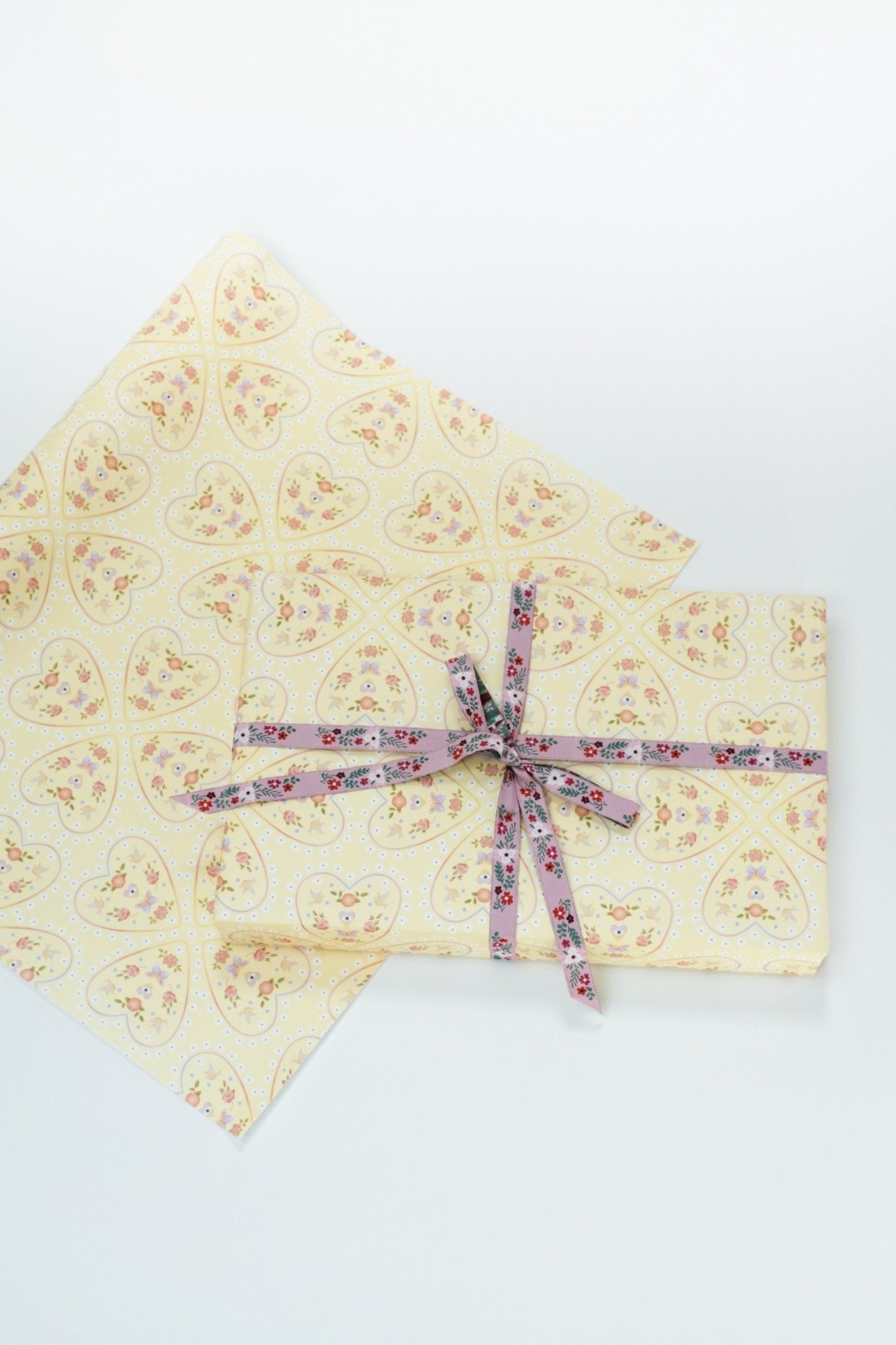 Single sheet of Mirrored Hearts gift wrap. Shown wrapped with purple floral ribbon.