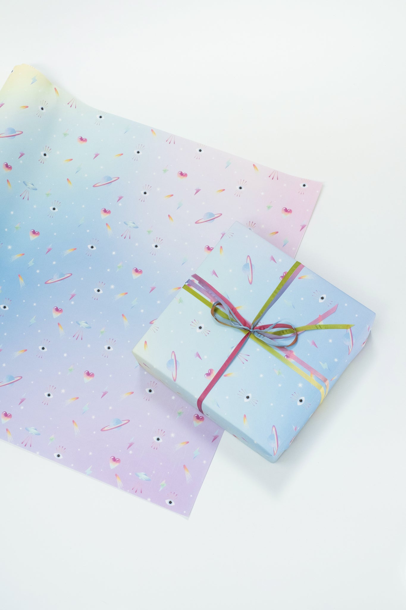 Single sheet of gift wrap with pastel gradient background and neon icons. Shown wrapped on present with pink and green velvet ribbon.
