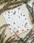 "Sending All Of My Love" pointillism font design aligned center surrounded by pressed flowers printed on cardstock among a background of cream colored cloth and lavender plants.