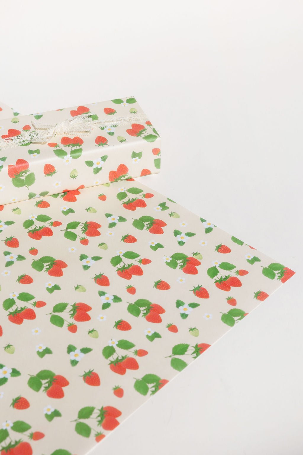Our Strawberry holiday gift wrap features red strawberries on a stem of two or three, surrounded by smaller and larger red or green strawberries and white flowers printed on a cream colored background.