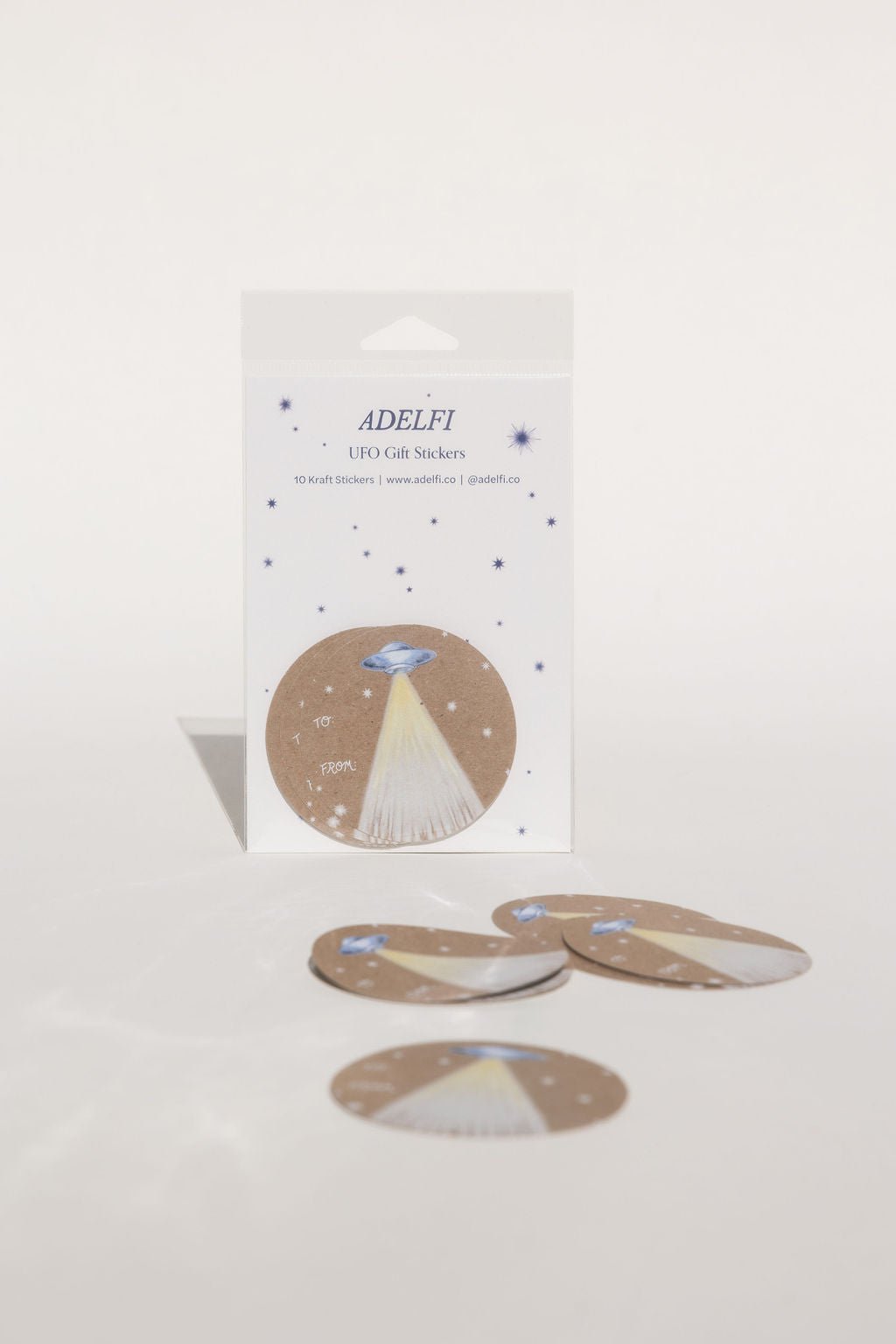 This Gift Sticker features a blue-silver UFO with a light beam surrounded by stars, with the words "To" and "From" written in cursive on the center left.
