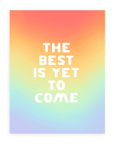 Rainbow gradient background with "The Best Is Yet To Come" in bold, white font printed on cardstock  resting on a white background.