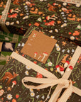 This gift tag features red magic mushrooms of varying height aligned diagonally in the upper left and lower right hand corners, with the words "To" and "From" in cursive all-caps font aligned center left. Shown on our Forest Creatures gift wrap.