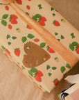 This Gift Sticker is heart-shaped with a red strawberry in the upper left hand corner, a green and red strawberry at the bottom, and a white flower with three leaves in the upper right corner, with the words "To" and "From" written in cursive in the center left. Shown on our Strawberries gift wrap.