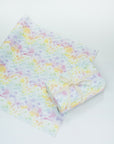 Sheet of rainbow clouds gift wrap beneath a present wrapped with rainbow clouds and a white ribbon.