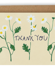 Three stems of lively white forest flowers cover the card nearly top to bottom horizontally, with the words "Thank You" going through the center of them in black ink. This design is printed on a cream colored background. Shown with Kraft envelope.