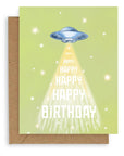 Greeting card with green background featuring stars and flying saucer with "happy birthday" printed down the front. Shown with kraft envelope.