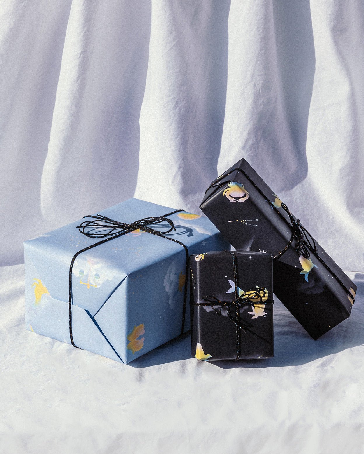 Presents wrapped with "Day" and "Night" horoscope gift wrap tied with black and white string against a fabric white background.