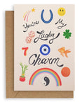 Cream colored card with various lucky items on the front: penny, goldfish, four leaf clover, dice, the number seven, bamboo plant, yin and yang, rainbow, horseshoe, shooting star, and smiley face with the words "You're My Lucky Charm" printed on cardstock. Shown with kraft envelope.