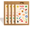 Four Lucky Charms sticker sheets with varying lucky items on a cream colored sheet with kraft packaging against a white background.