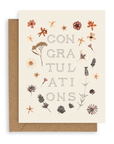 Cream colored background with "Congratulations" in  pointillism-style center aligned font printed on cardstock resting on a kraft envelope.