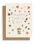 A cream colored card with dried flowers scattered and the words "Happy Birthday!" printed on the cardstock. Shown with kraft envelope.