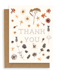 Various pressed flowers arranged around the words "thank you" in black pointilistic font printed on a cream background. Shown with kraft envelope.