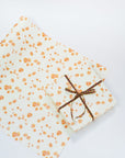 Single sheet of cream colored gift wrap with printed orange California Poppies on top. Shown wrapped with plaid ribbon.